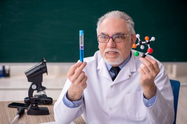 Old chemist teacher sitting in the classroom