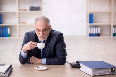 Old employee drinking tea at workplace