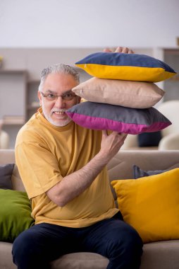 Evde bir sürü yastığı olan yaşlı bir adam.
