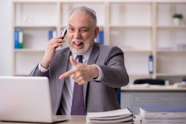 Old employee speaking by phone at workplace