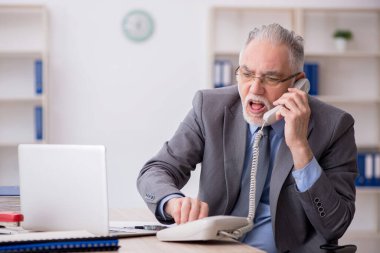 Old employee speaking by phone at workplace