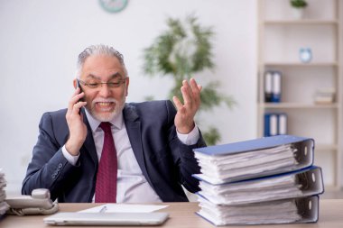 Old employee speaking by phone at workplace