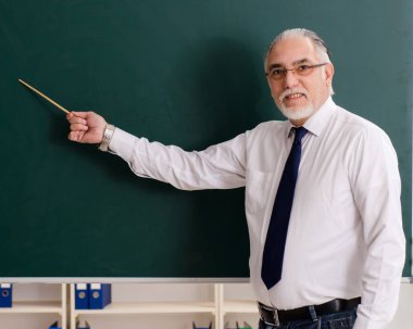 Tahtanın önündeki yaşlı erkek öğretmen.