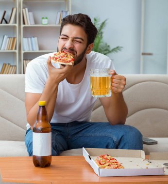 Pizza yiyen adam evde yemek yiyor, dinleniyor.