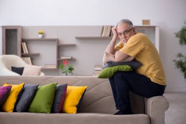Evde bir sürü yastığı olan yaşlı bir adam.