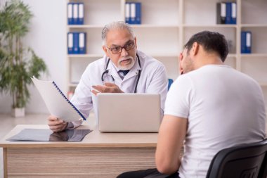 Genç hasta yaşlı doktoru ziyaret ediyor.