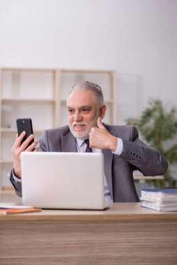 Old employee speaking by phone at workplace