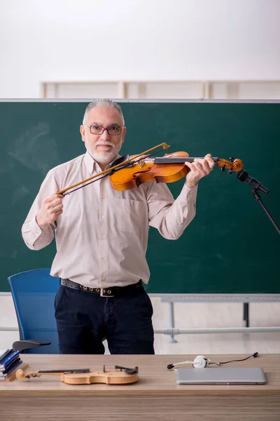 Old teacher playing violin in the classroom