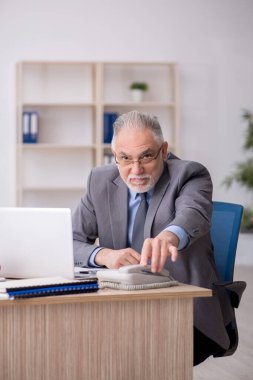 Old employee speaking by phone at workplace