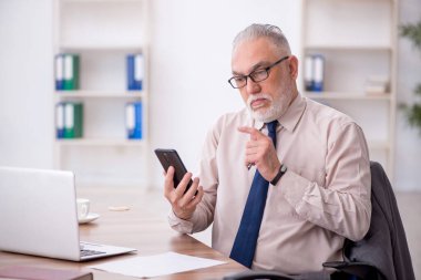 Old employee speaking by phone at workplace