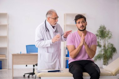 Genç hasta yaşlı erkek doktoru ziyaret ediyor.