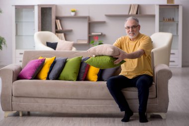 Evde bir sürü yastığı olan yaşlı bir adam.