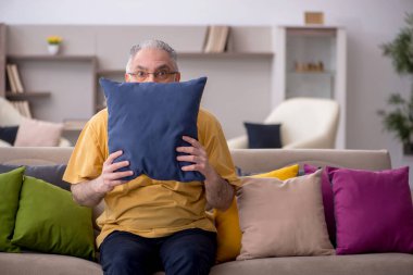 Evde bir sürü yastığı olan yaşlı bir adam.