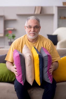 Evde bir sürü yastığı olan yaşlı bir adam.