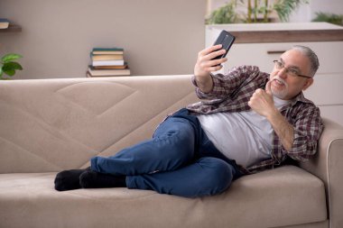 Yaşlı adam salgın sırasında evde telefonla konuşuyor.