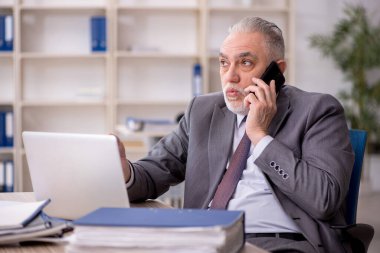 Old employee speaking by phone at workplace