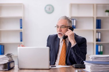 Old employee speaking by phone at workplace