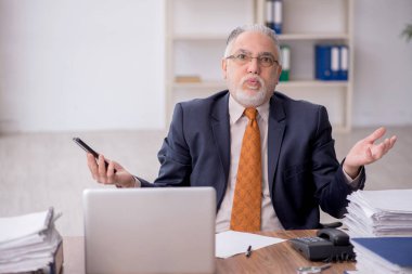 Old employee speaking by phone at workplace