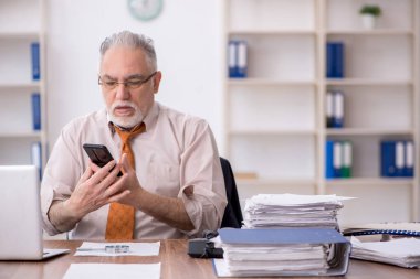 Old employee speaking by phone at workplace