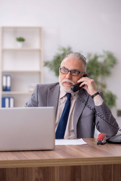 Old employee speaking by phone at workplace