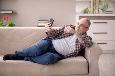 Yaşlı adam salgın sırasında evde telefonla konuşuyor.