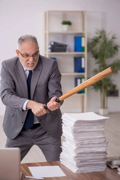 Old employee holding baseball bat at workplace