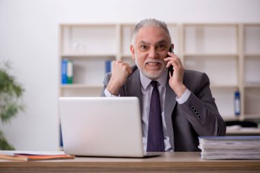 Old employee speaking by phone at workplace
