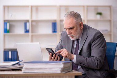 Old employee speaking by phone at workplace