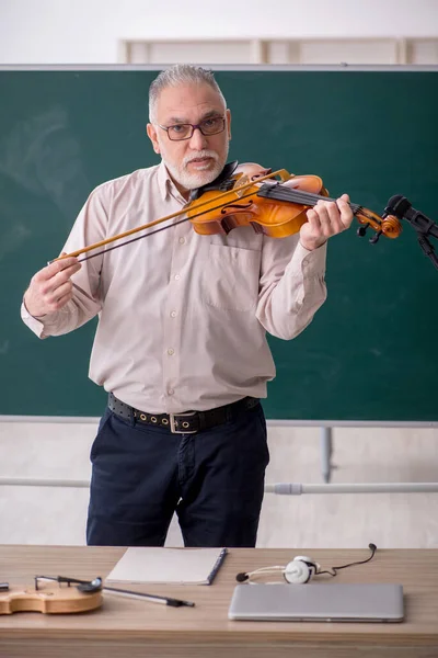 Old teacher playing violin in the classroom