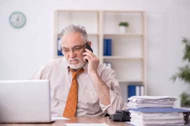 Old employee speaking by phone at workplace