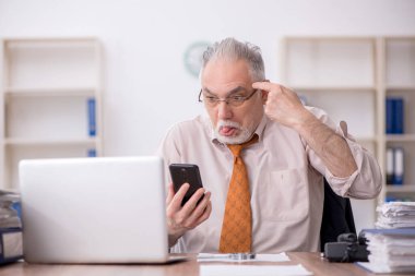 Old employee speaking by phone at workplace