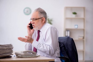 Old employee speaking by phone at workplace