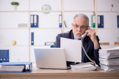 Old employee speaking by phone at workplace