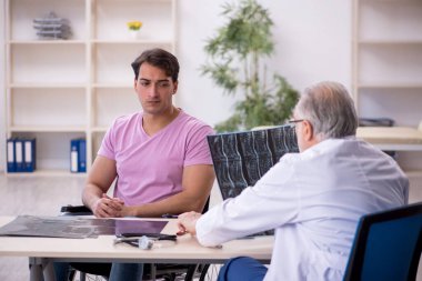 Tekerlekli sandalyedeki genç adam yaşlı doktor radyoloğu ziyaret ediyor.