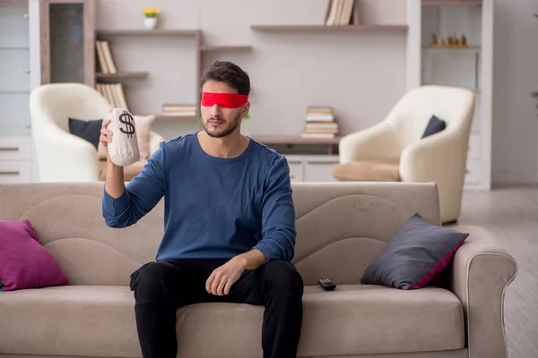 Blindfolded man holding moneybag at home