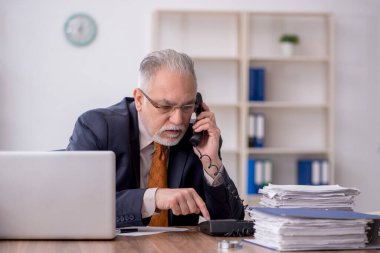 Old employee speaking by phone at workplace