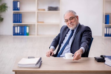 Old employee drinking tea at workplace