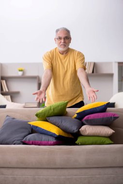 Evde bir sürü yastığı olan yaşlı bir adam.