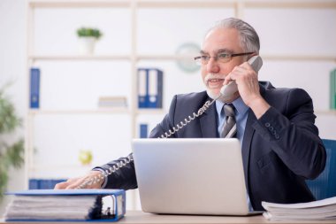 Old employee speaking by phone at workplace