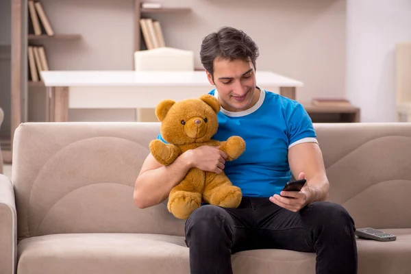 Young man sitting with bear toy at home