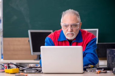 Sınıfta bilgisayar tamir eden yaşlı bir erkek tamirci.