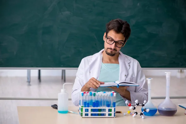 Young chemist in front of blackboard