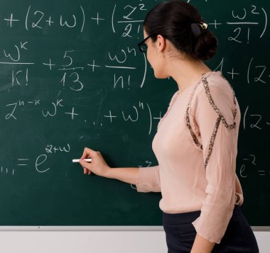 Kadın öğretmen karatahtanın önünde duruyor.