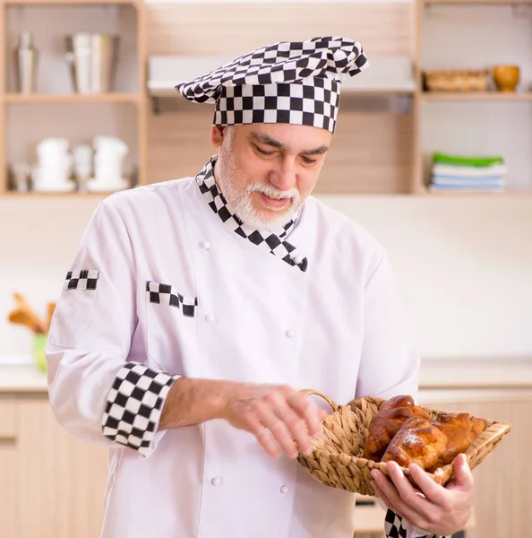 The old male baker working in the kitchen