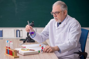 Old chemist teacher sitting in the classroom