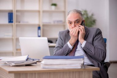Old employee speaking by phone at workplace