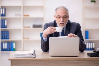 Old employee drinking tea at workplace