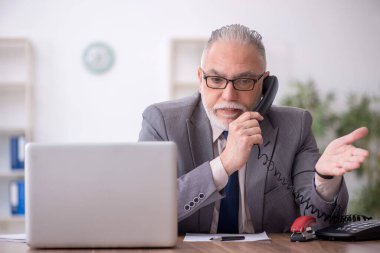 Old employee speaking by phone at workplace