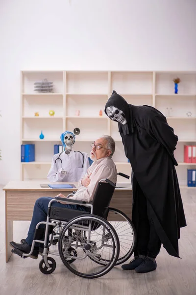 Old male patient in wheel-chair visiting two devil doctors