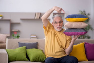 Evde bir sürü yastığı olan yaşlı bir adam.